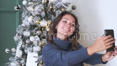 在圣诞树的背景下，用手机拍下迷人的深色头发的自拍